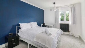 Ein Schlafzimmer mit Bett, Schreibtisch und einem fenster mit Vorhängen.