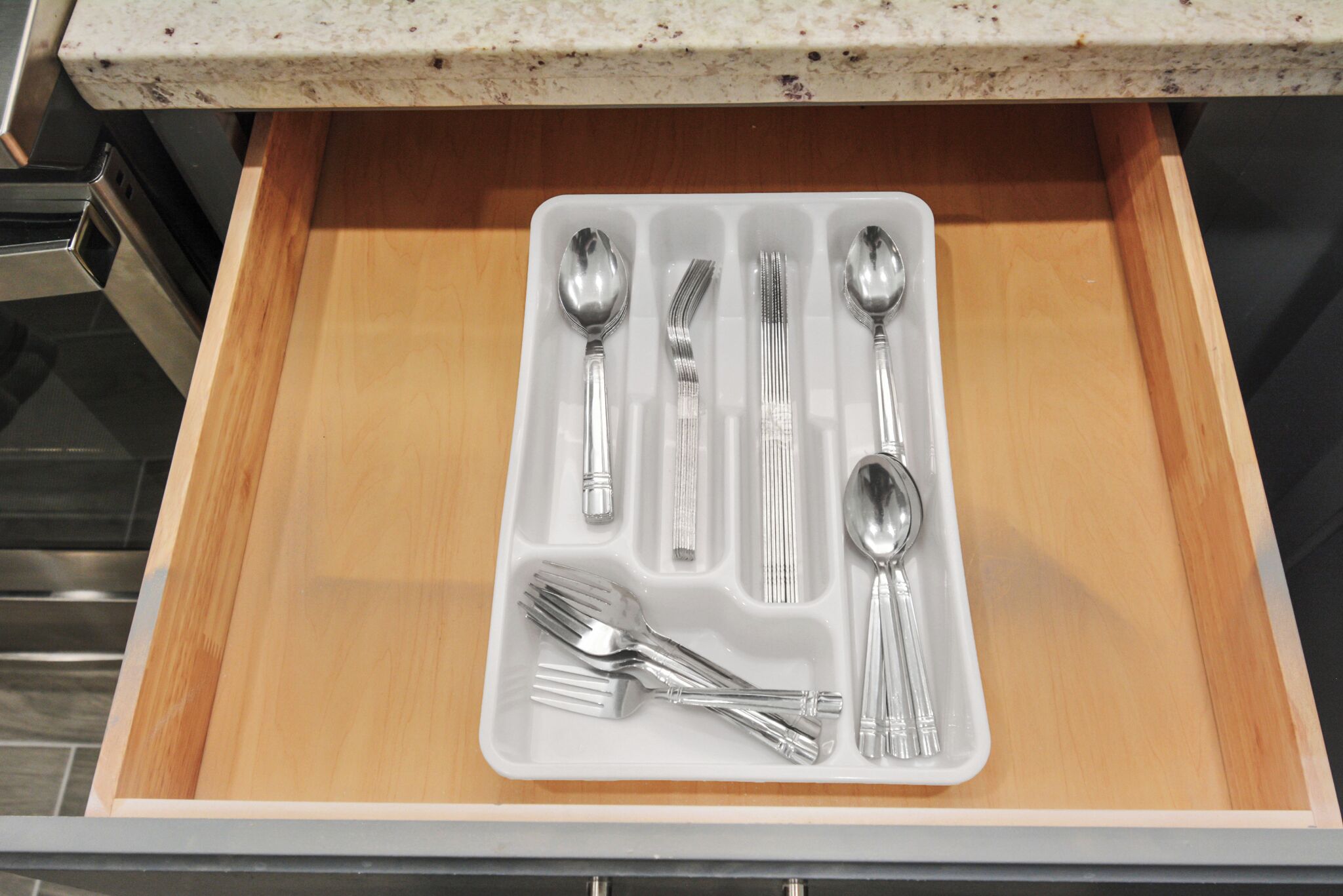 A drawer containing a set of silverware including forks, spoons, and a knife.