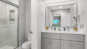 A modern bathroom with a glass shower enclosure, a toilet, and a vanity with a mirror and hairdryer. - Near Disney, Universal, Outlets & OCCC (Orlando)