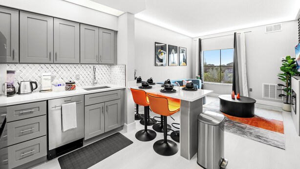 A modern kitchen with grey cabinets, a white countertop, and a bar area with orange stools. - Near Disney, Universal, Outlets & OCCC (Orlando)