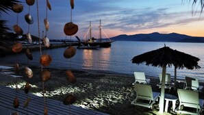 A beach with lounge chairs, a thatched umbrella, and a boat docked near the shore.