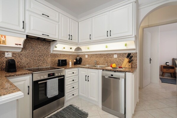 Cocina moderna con armarios blancos, encimeras de granito y electrodomésticos de acero inoxidable, incluyendo un horno empotrado.
