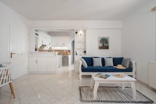 A modern living room with a white sofa, a coffee table, and a kitchen in the background.