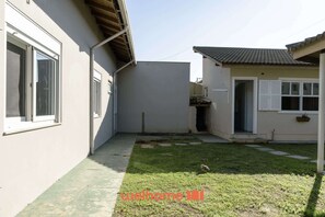 A narrow courtyard with a small lawn, a white building with a tiled roof, and a door with a window.