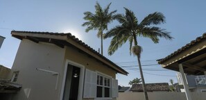 A small, single-story building with a tiled roof and a door leading to a dark interior. There are palm trees in the background, and the sky is clear.