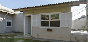 Ein kleines Haus mit hellbeiger Fassade, weißen Fensterläden und einem kleinen Fenster.