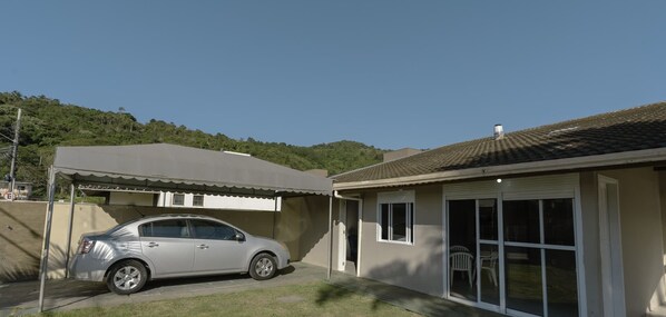 A single-story house with a car parked in the driveway, a covered patio area, and a view of a hillside.