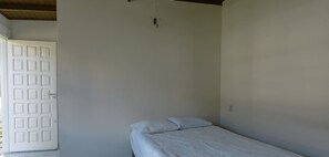 A small, single-bed room with a plain white wall and a door.