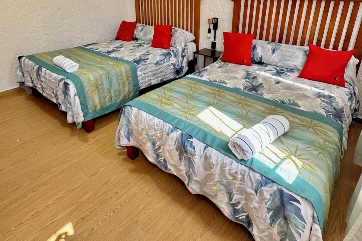 A room with two wooden beds, each with a floral bedspread and red pillows.