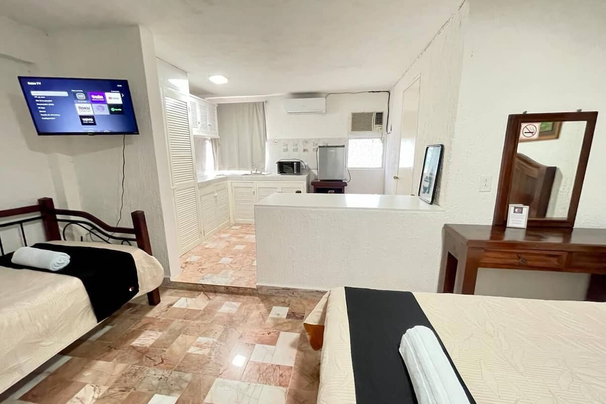 A hotel room with two beds, a TV, a kitchenette, and a bathroom.