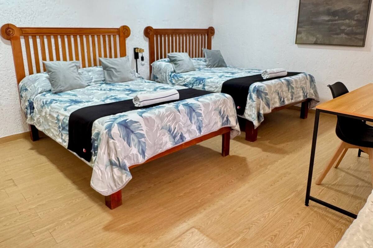 A room with two wooden beds, a wooden table, and a painting on the wall.