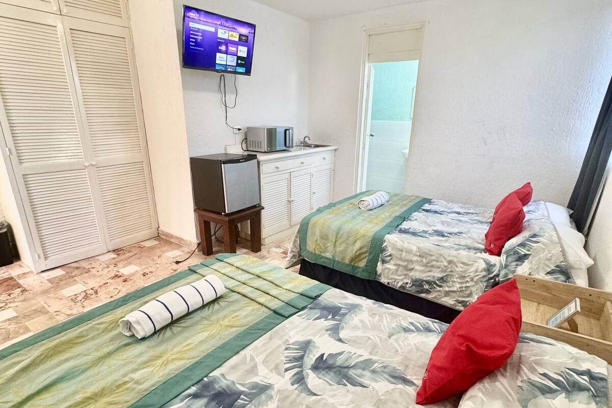 A hotel room with two beds, a television, a desk with a microwave, and a bathroom visible through an open door.