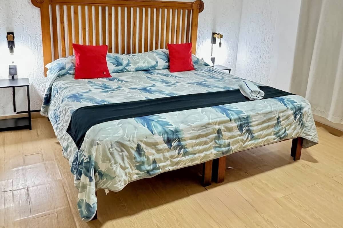 A bedroom with a wooden bed frame, a floral bedspread, and two red pillows.