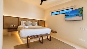 Une chambre moderne avec un grand lit, un banc en bois, un téléviseur fixé au mur et une fenêtre donnant sur la plage.