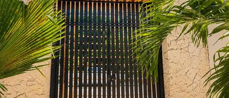 A building with a textured facade, a black gate, and surrounding greenery.