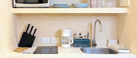 Una cocina compacta con microondas, tostadora, licuadora y lavamanos.
