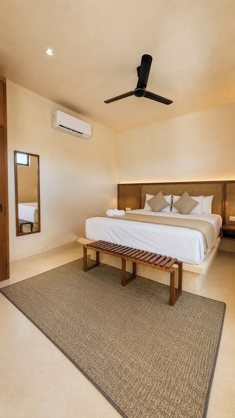 A bedroom with a bed, a bench, a ceiling fan, an air conditioning unit, and a mirror.