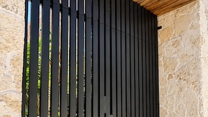 A black metal gate with vertical slats, a stone wall, and a wooden ceiling. -  Lapso At Tulum (Tulum)