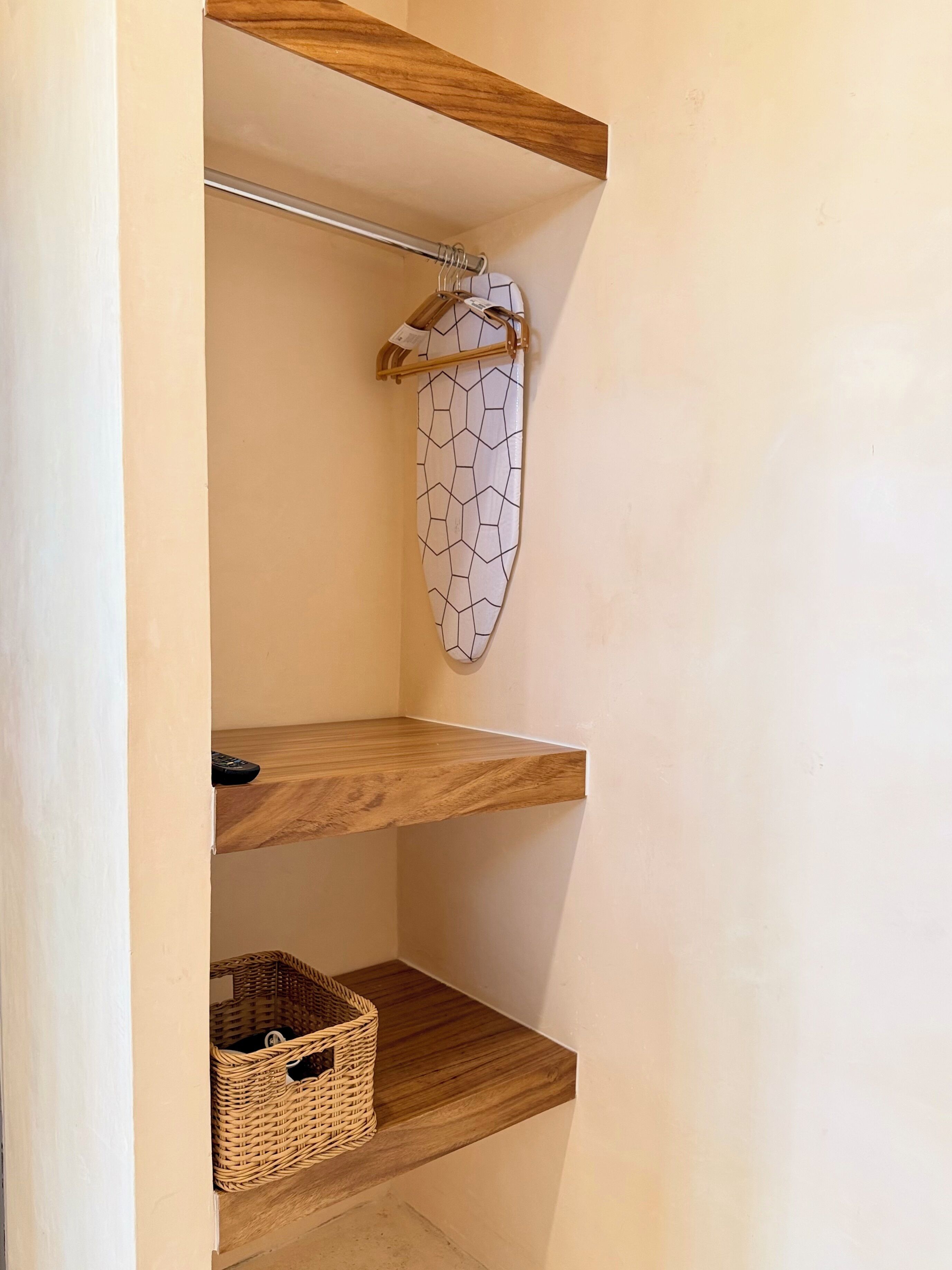Un coin de pièce avec une étagère en bois, un tissu à motifs suspendu et un panier en osier.