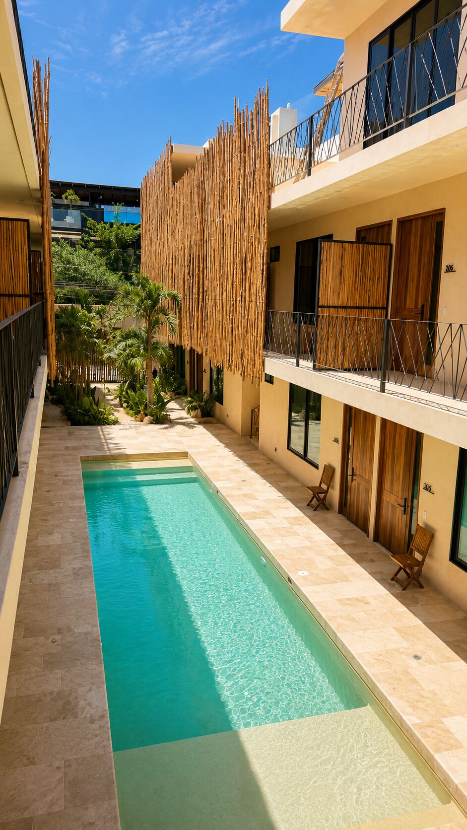A pool area with a clear blue pool, a bamboo fence, and a building with balconies.