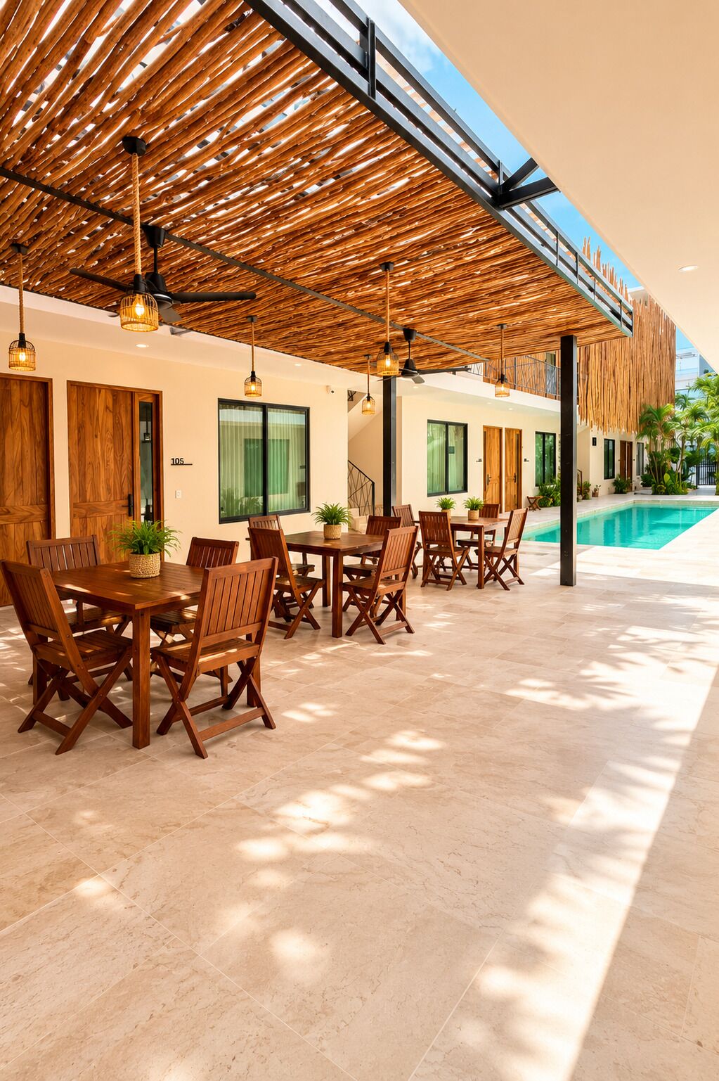 A covered outdoor dining area with wooden tables and chairs, a pool, and a view of the sky.