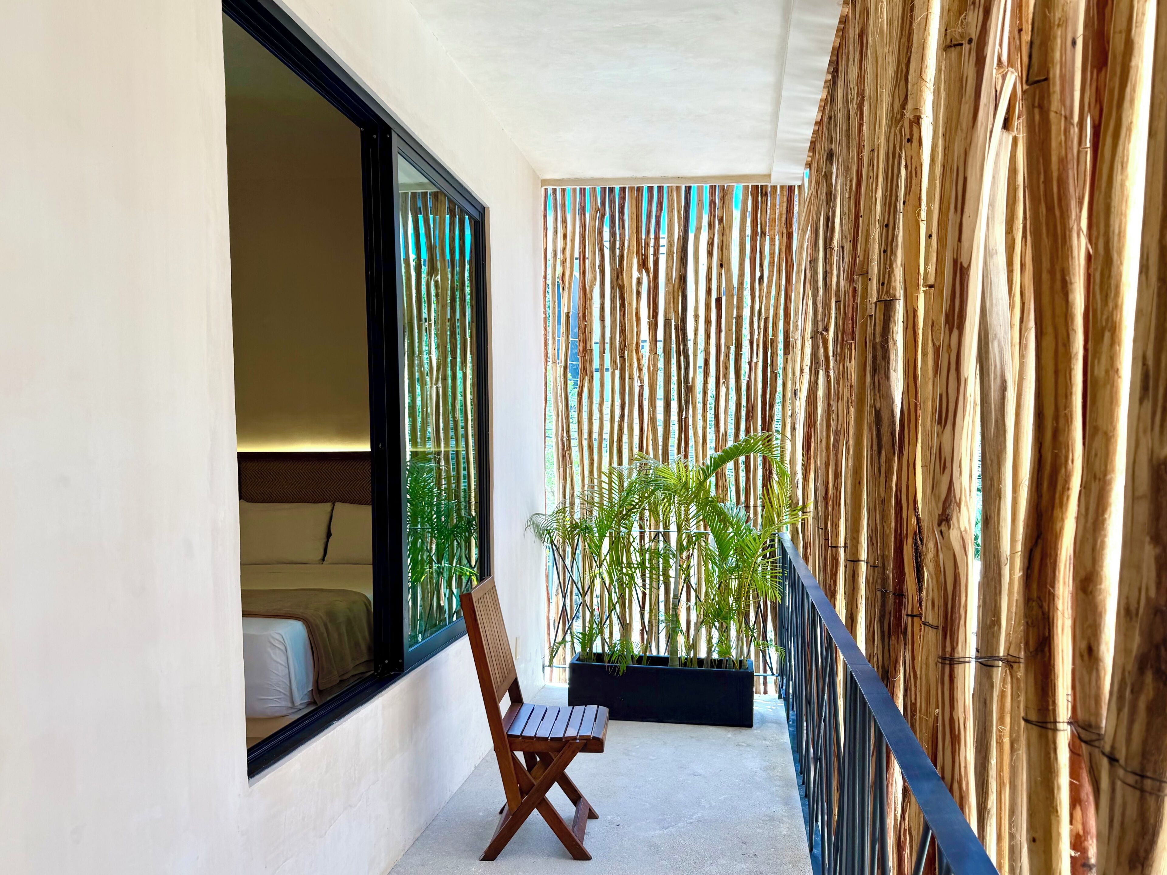 A balcony with a wooden chair, a potted plant, and a bamboo wall.