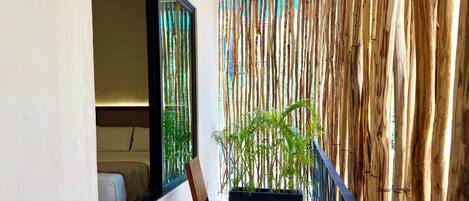 A balcony with a wooden chair, a potted plant, and a bamboo wall.