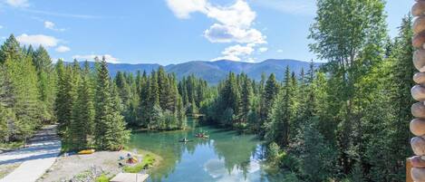 A serene lake surrounded by dense forest, with a clear sky and distant mountains.