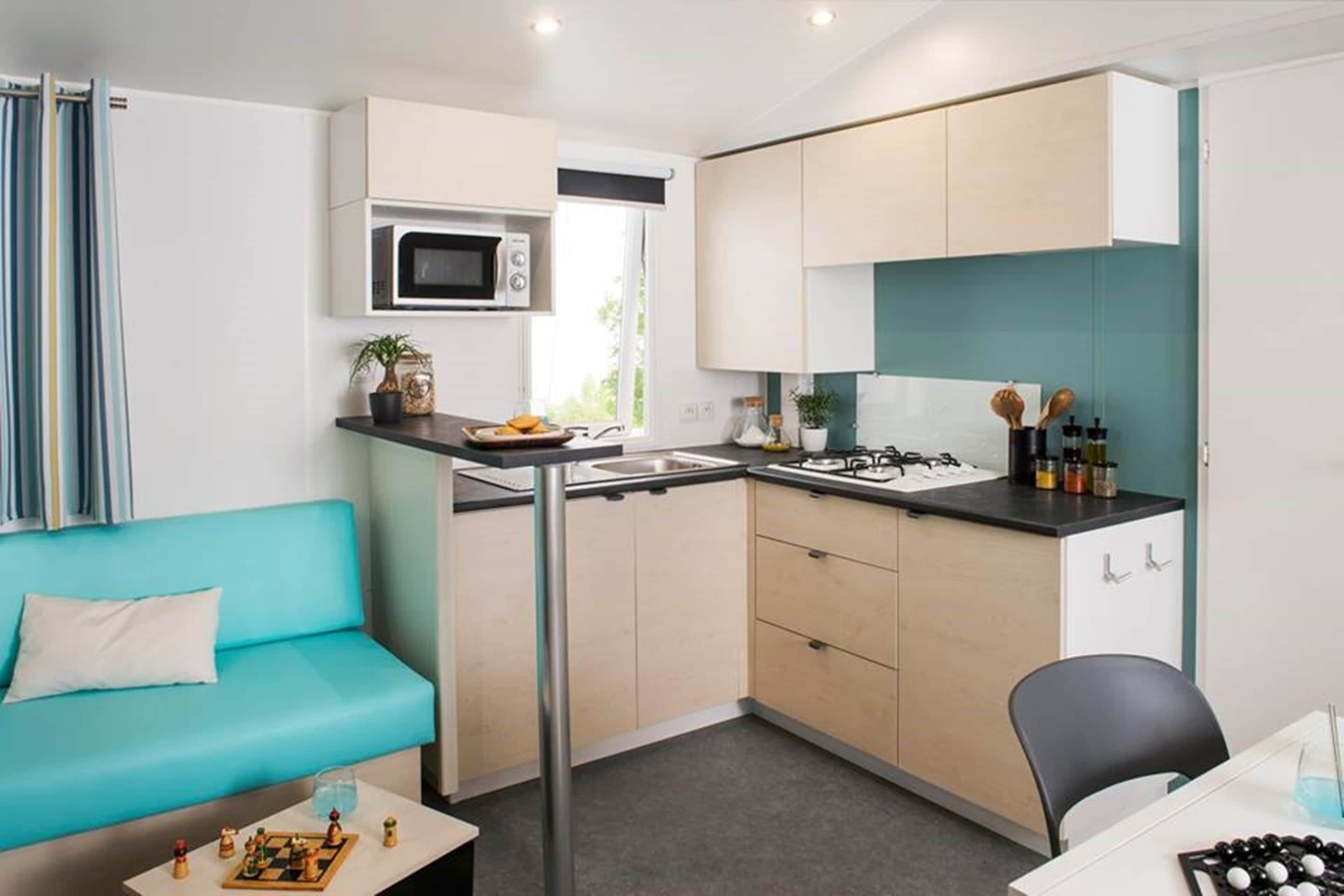 A compact kitchen with a microwave, sink, and stove, a teal sofa, and a small dining table.