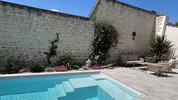 Une piscine avec des murs en pierre et des meubles d’extérieur.