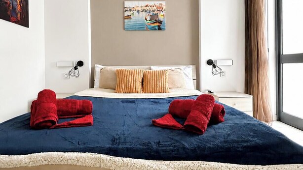 Habitación de hotel con una cama grande, dos almohadas, un cuadro en la pared y una ventana con cortinas.
