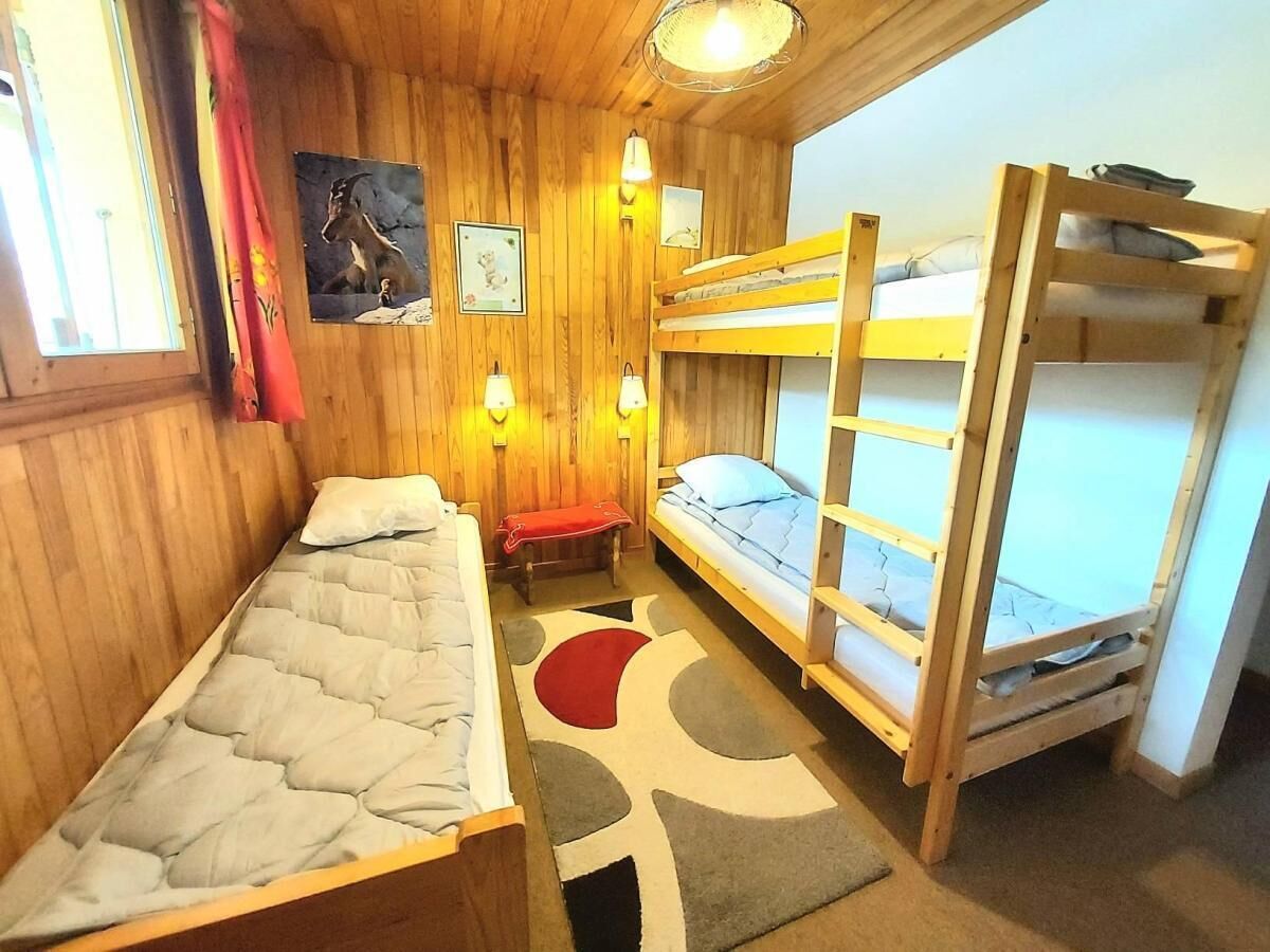 A small, cozy room with wooden walls and bunk beds. There are wall-mounted lights and a small bench.