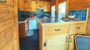 Interno di una baita in legno con angolo cottura, caratterizzato da mobili in legno, zoccolo piastrellato e isola centrale con cassetti.