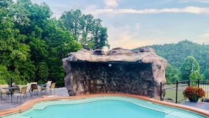 A swimming pool with a natural rock formation, surrounded by outdoor seating and lush greenery.
