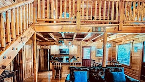 A cabin interior with a wooden staircase, a dining area, and a living room with a sofa.
