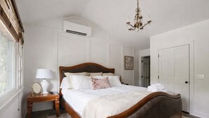 Une chambre à coucher bien aménagée, avec un lit en bois, une table de chevet avec une lampe, un appareil de climatisation et un lustre.