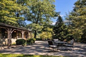 Un edificio rústico con un patio cubierto, asientos al aire libre y vistas a árboles circundantes.