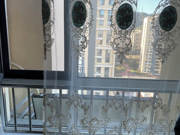 A window with ornate lace curtains and a view of high-rise buildings.
