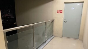 A corridor with a glass railing, a door with a sign, and a cityscape view at night.