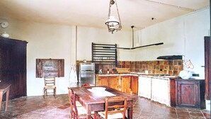 Une cuisine avec une table en bois, des chaises, un luminaire suspendu et un sol carrelé.
