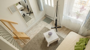 A bedroom with a bed, a small white table with a purple flower, a wooden chair, a mirror, and a window with a view of a balcony. - Sidi Studio - left side, right in the heart of Budapest, The Sidonies Twins in Seventh (Budapest)