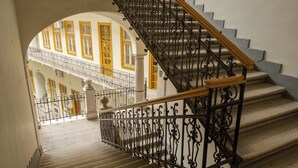 A staircase with ornate black iron railings and a wooden handrail, leading to an upper floor with yellow-framed windows and a balcony. - Sidi Studio - left side, right in the heart of Budapest, The Sidonies Twins in Seventh (Budapest)