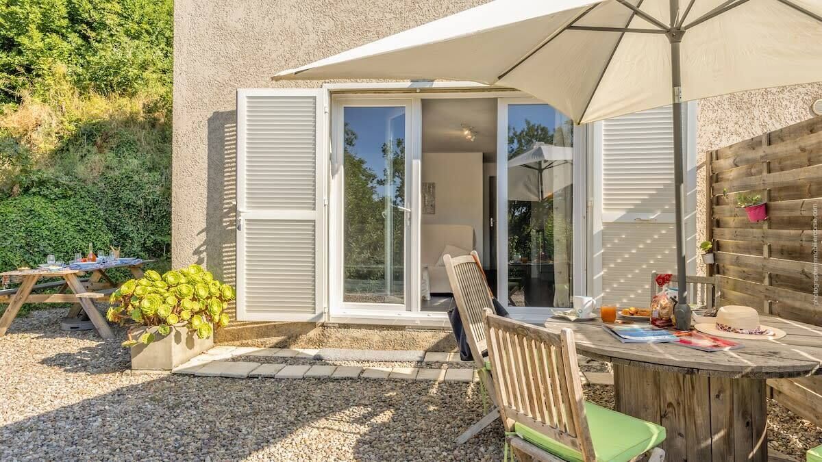 Un patio con mesa de madera, sillas y una sombrilla grande.