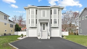Une maison à deux étages avec une entrée centrale, un porche à l’avant et une allée.