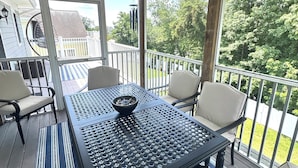 Une terrasse extérieure couverte, avec une table et des chaises, un luminaire suspendu et une vue sur un quartier résidentiel avec des arbres et une clôture.