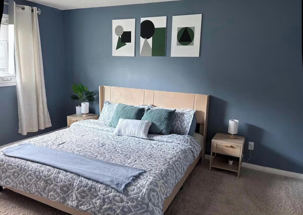 A bedroom with a bed, nightstands, a potted plant, and artwork on the wall.