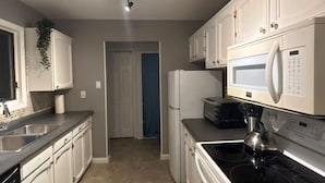 Una cocina con armarios blancos, estufa, microondas y refrigerador.