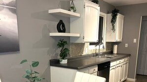 Una cocina moderna con gabinetes blancos, encimera de acero inoxidable y mesa de comedor de vidrio.