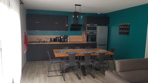 A modern kitchen with a dining area, featuring a wooden table, chairs, and a teal accent wall. - New house for vacations in Charente-Maritime (Saint-Agnant)