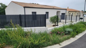 A modern two-story house with a white exterior and a tiled roof, surrounded by a black fence and lush greenery. - New house for vacations in Charente-Maritime (Saint-Agnant)